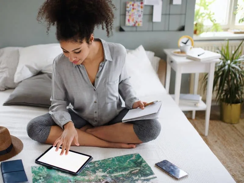 A nanny using a scheduling app on her phone while writing in a planner.