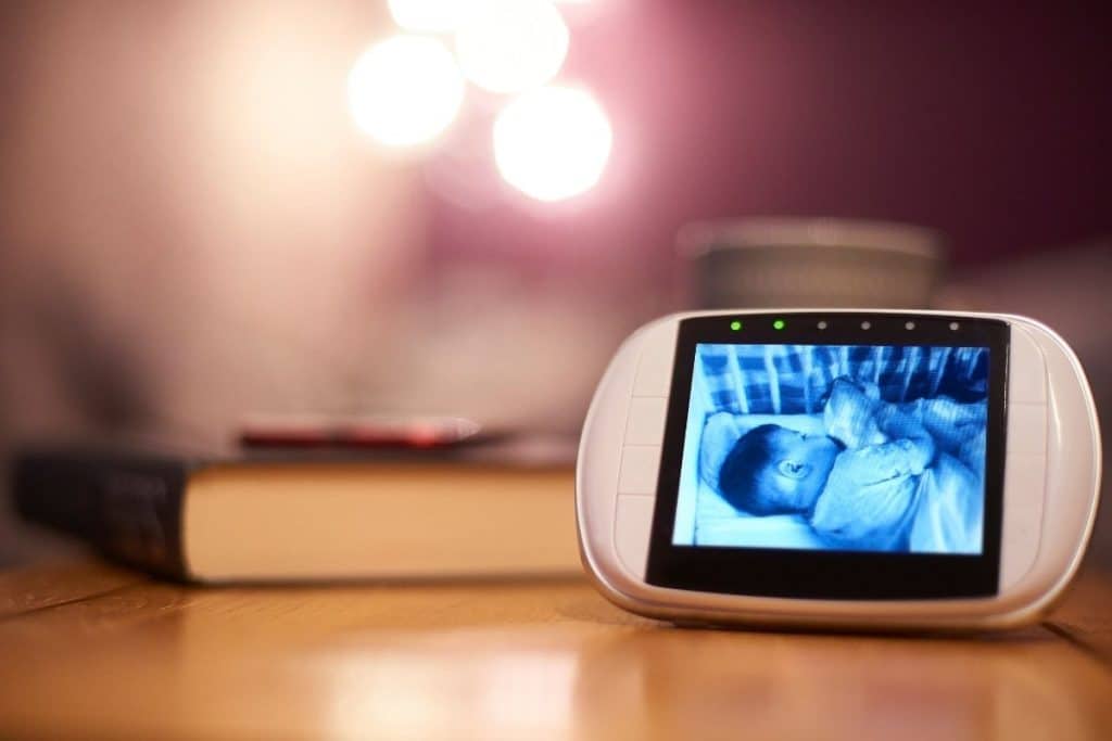 Awake nanny monitoring a newborn overnight with a notebook and baby monitor