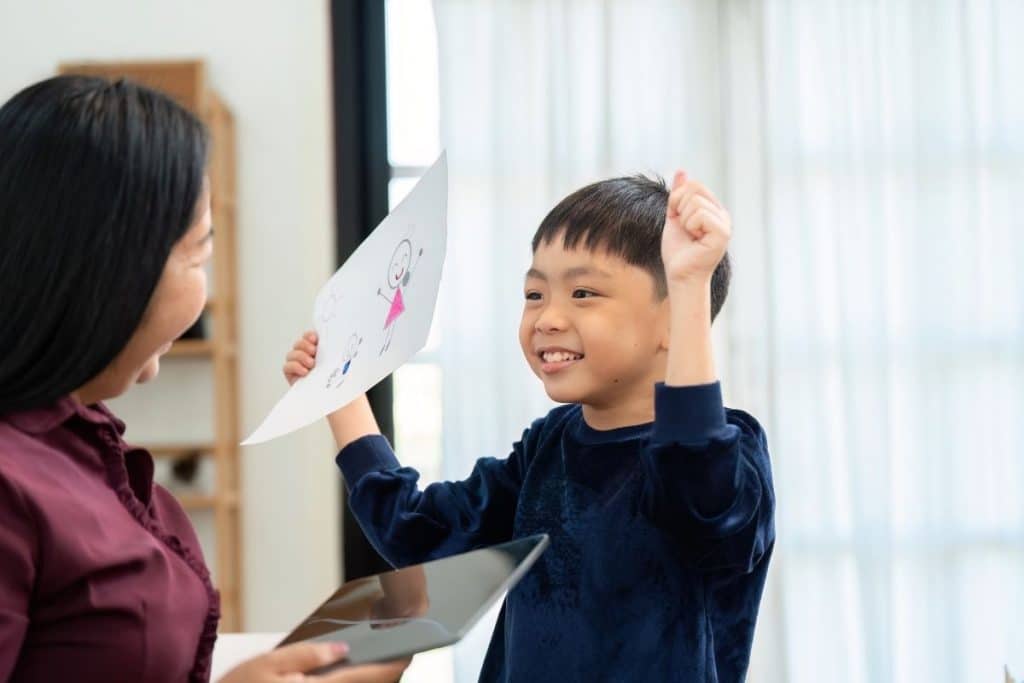 Child proudly showing artwork while parent praises effort