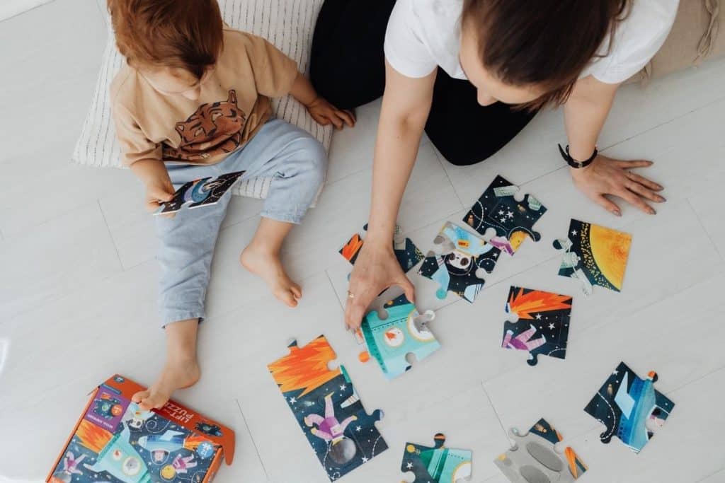 Child solving a puzzle with encouragement from nanny