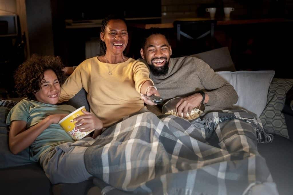 Family sitting on a couch with blankets, watching a movie together at home.