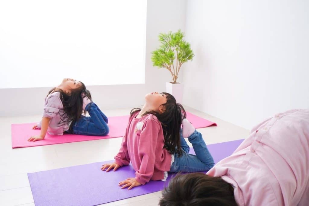 Parents, children, and nanny sitting on yoga mats doing mindfulness exercises at home.