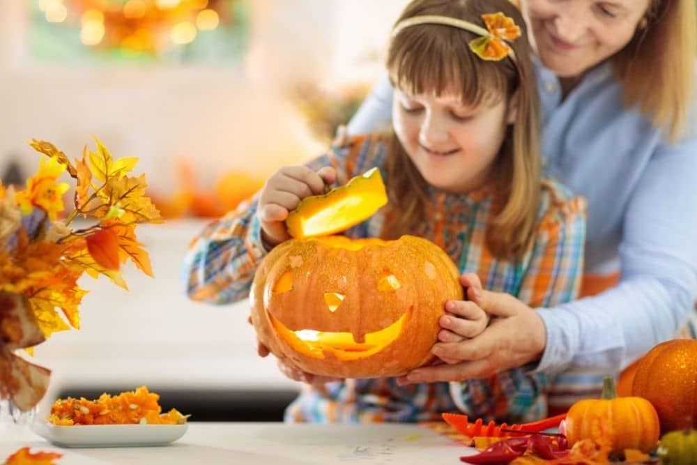 Nanny helping children carve pumpkins safely for Halloween.
