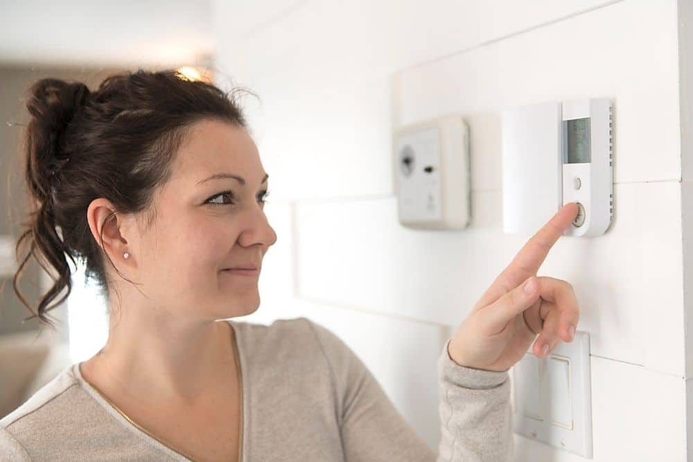 A family adjusting a home thermostat and checking smoke detectors in autumn.