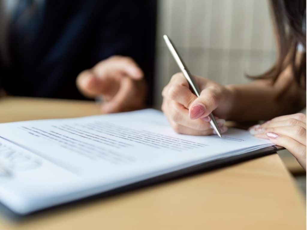 Close-up of hands signing a nanny employment contract on a wooden table.