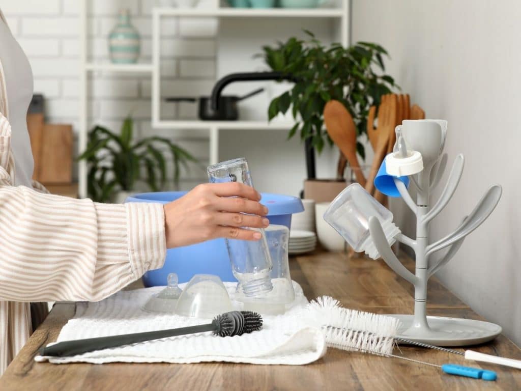 Nanny washing baby bottles in a clean home kitchen, emphasizing hygiene and safety.