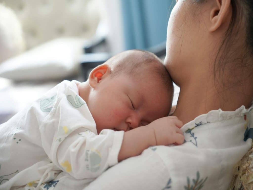 Newborn care specialist observing baby’s sleep and feeding routine while taking notes.