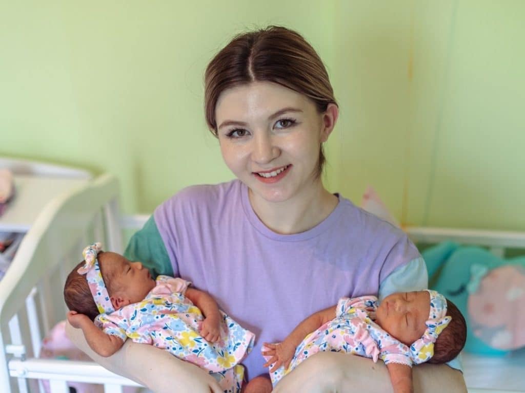 Professional night nanny holding twin infants in a peaceful nursery.