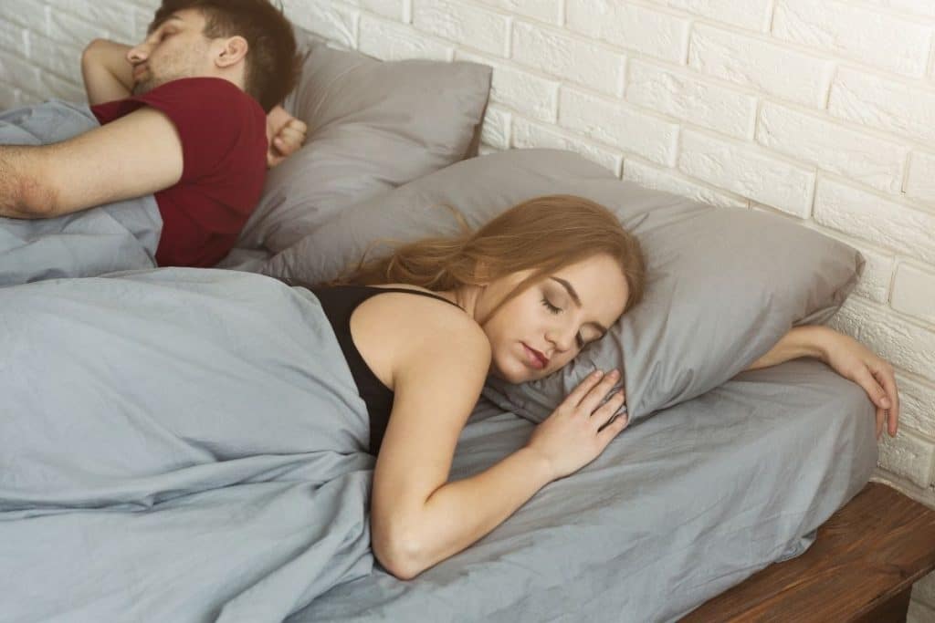 Parents sleeping peacefully while a professional night nanny tends to their baby in another room.