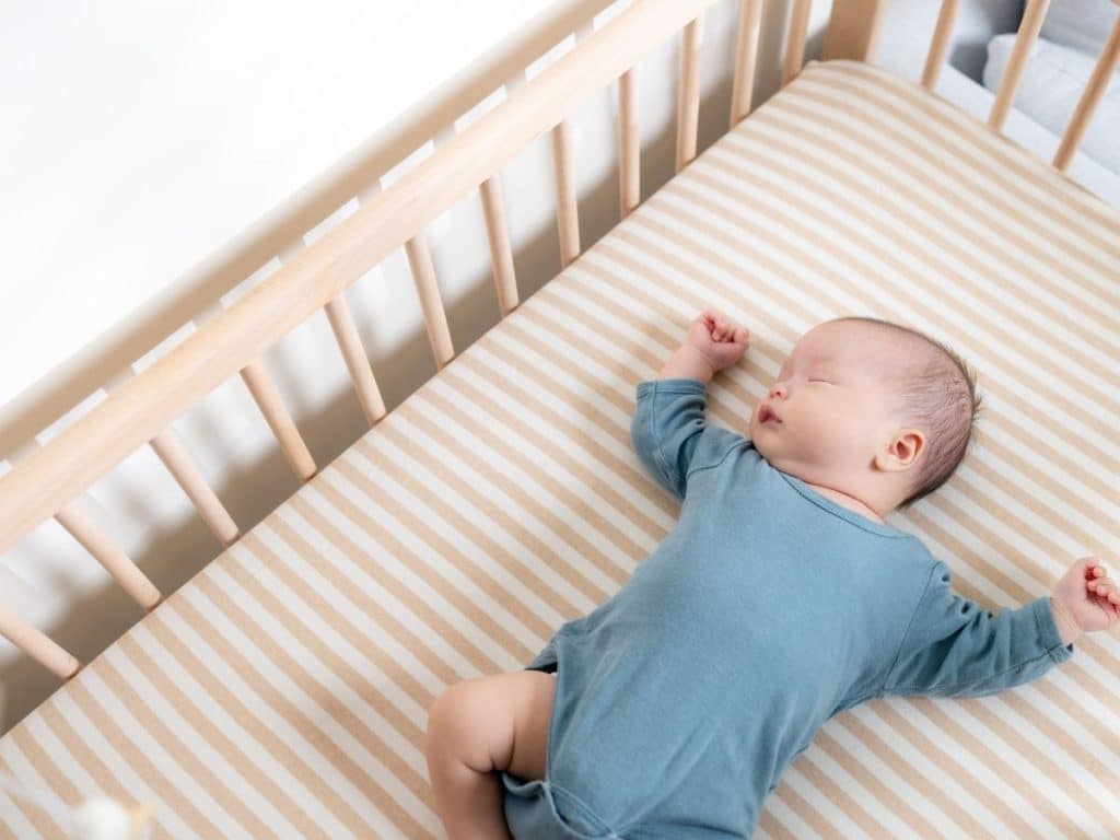 Newborn sleeping safely on their back in a minimalist, safe crib setup.
