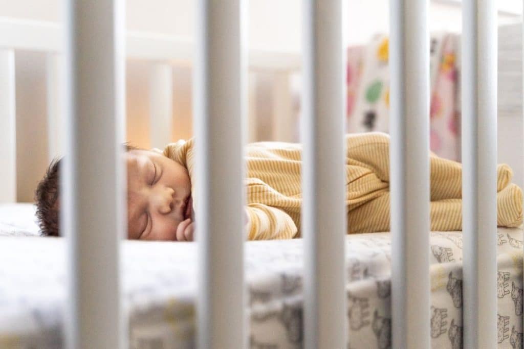 Newborn baby sleeping safely on their back in a clean, well-prepared crib with a soft night light.
