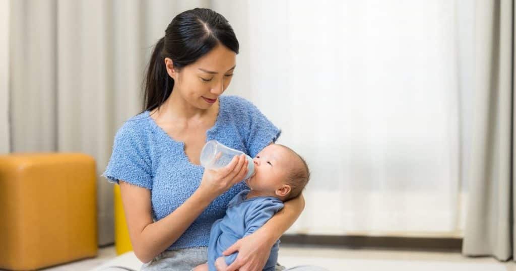Overnight nanny feeding newborn bottle while parents rest in Houston home