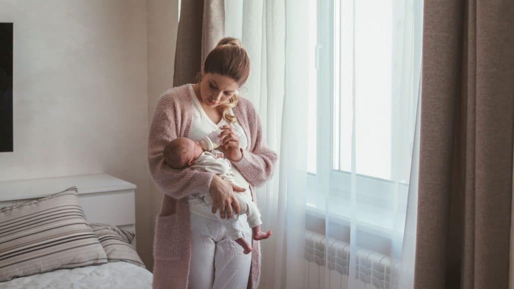 Night nanny feeding a newborn during a quiet overnight shift with calm lighting and organized nursery tools.