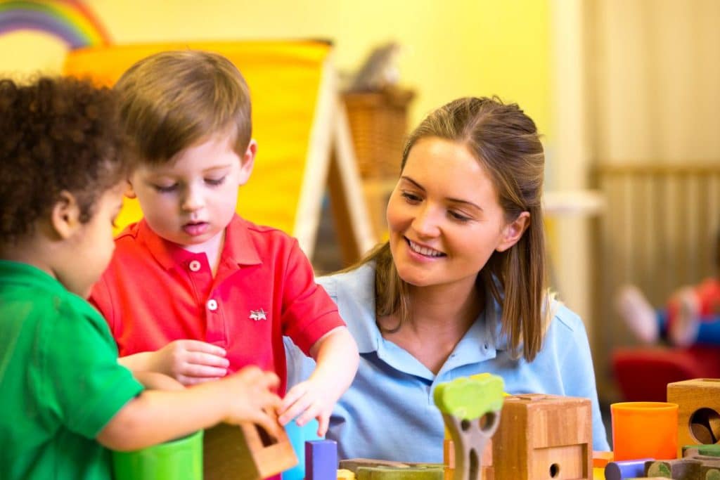 Professional nanny encouraging cooperation, sharing, and social development during children's playtime.